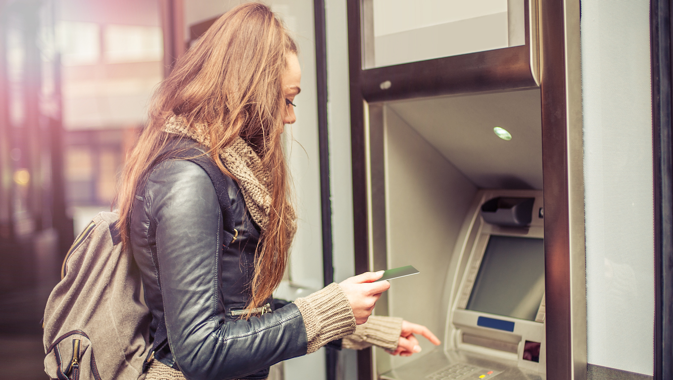 Young woman taking money from ATM, credit card