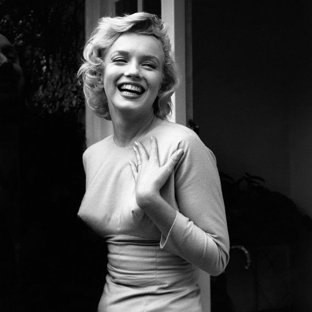 Marilyn Monroe wears a fitted dress and laughs. 