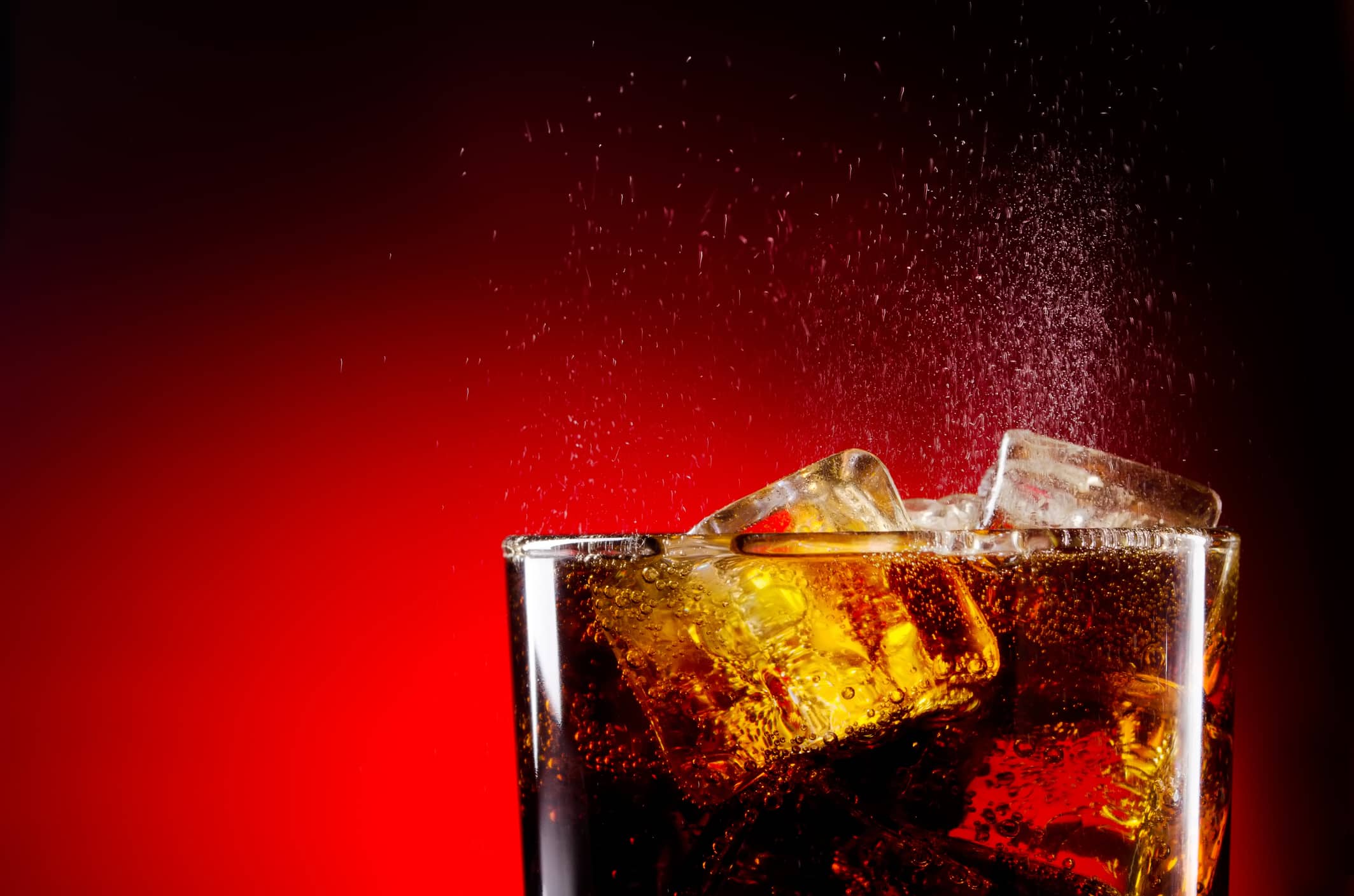 Glass cup of iced cola on red background
