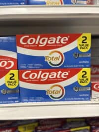 A retail shelf stocked with multiple red, white, and blue Colgate Total Whitening toothpaste boxes, each marked as a '2 VALUE PACK'. The boxes prominently display '24 HR Antibacterial Protection' and state 'Anticavity, Antigingivitis and Antisensitivity Toothpaste'.