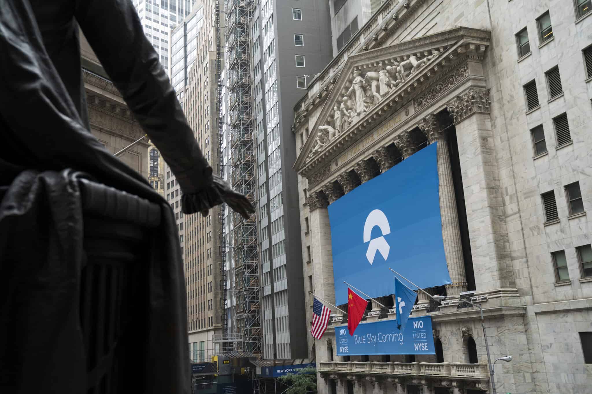 A view from behind the dark silhouette of a statue showing the New York Stock Exchange building. The NYSE facade features a large blue banner with the white NIO