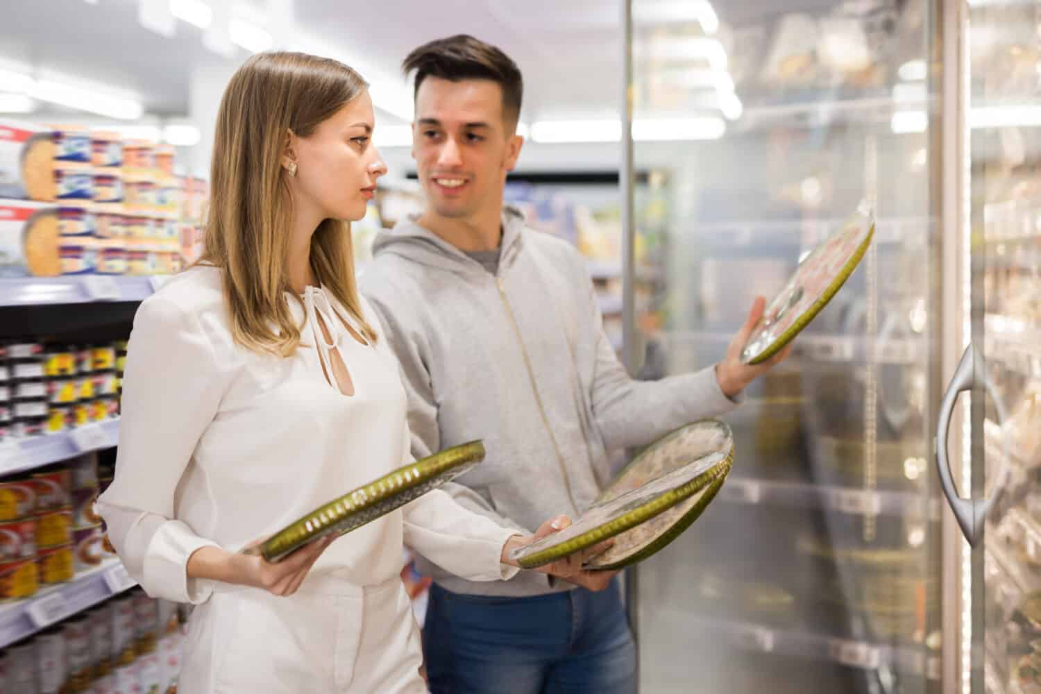 Young woman and man buying frozen pizza at grocery store
