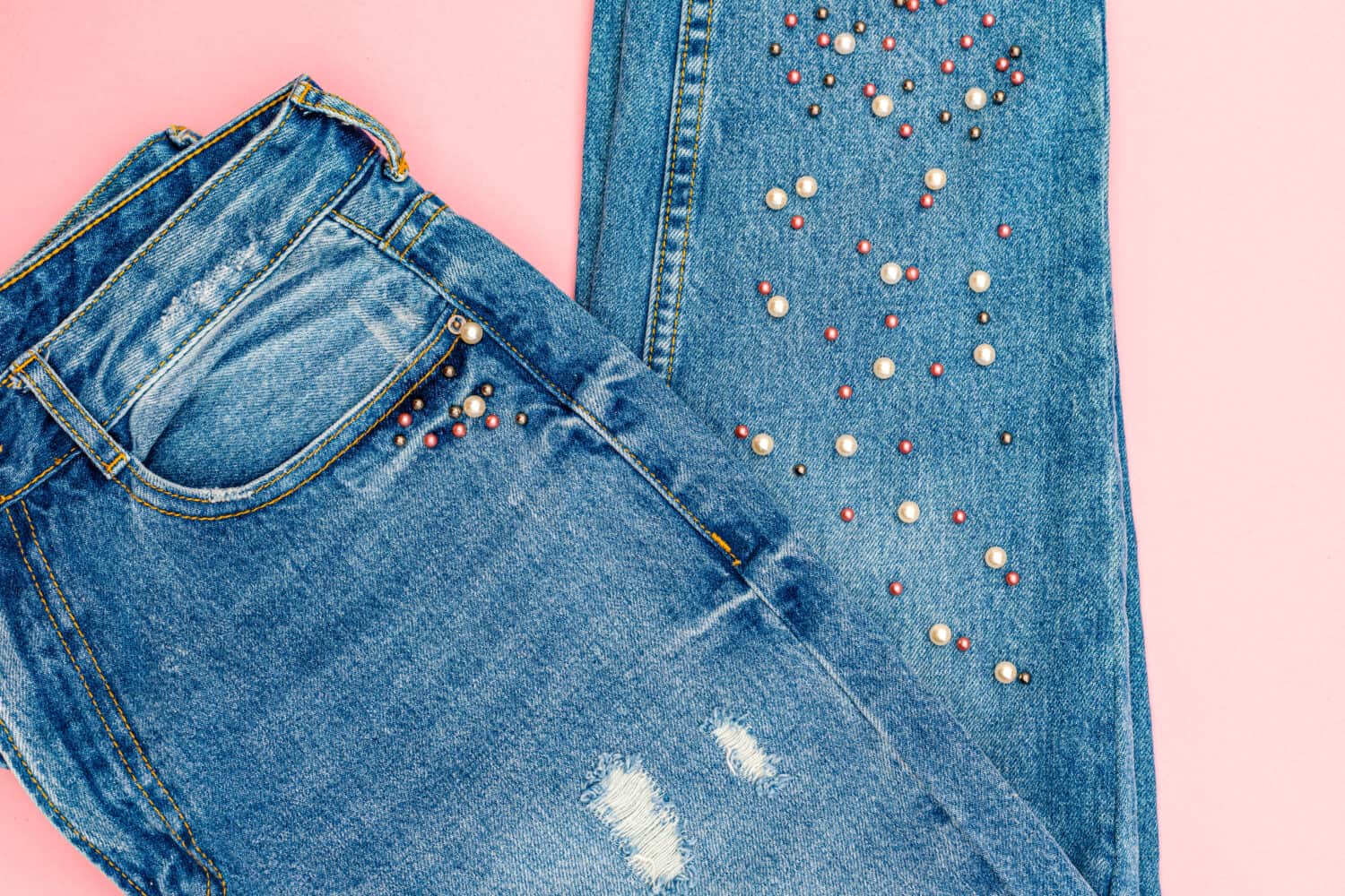 Denim jeans pants with beads on pink surface. Ripped Destroyed Torn Blue denim cloth background.