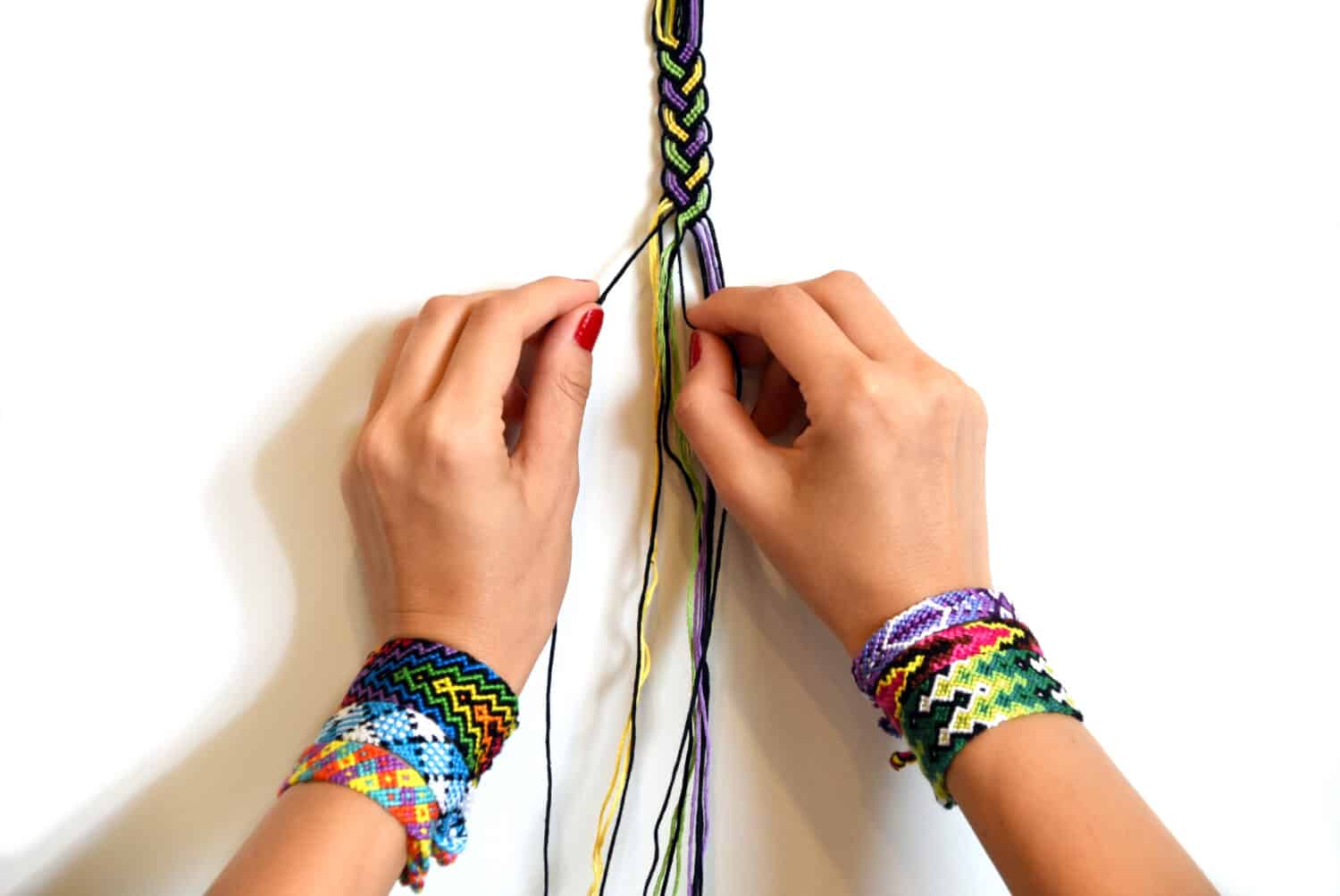 Process of weaving knot for DIY friendship bracelet Pigtail. Female hands with many handmade bracelets on wrists. step by step. White background with copy space