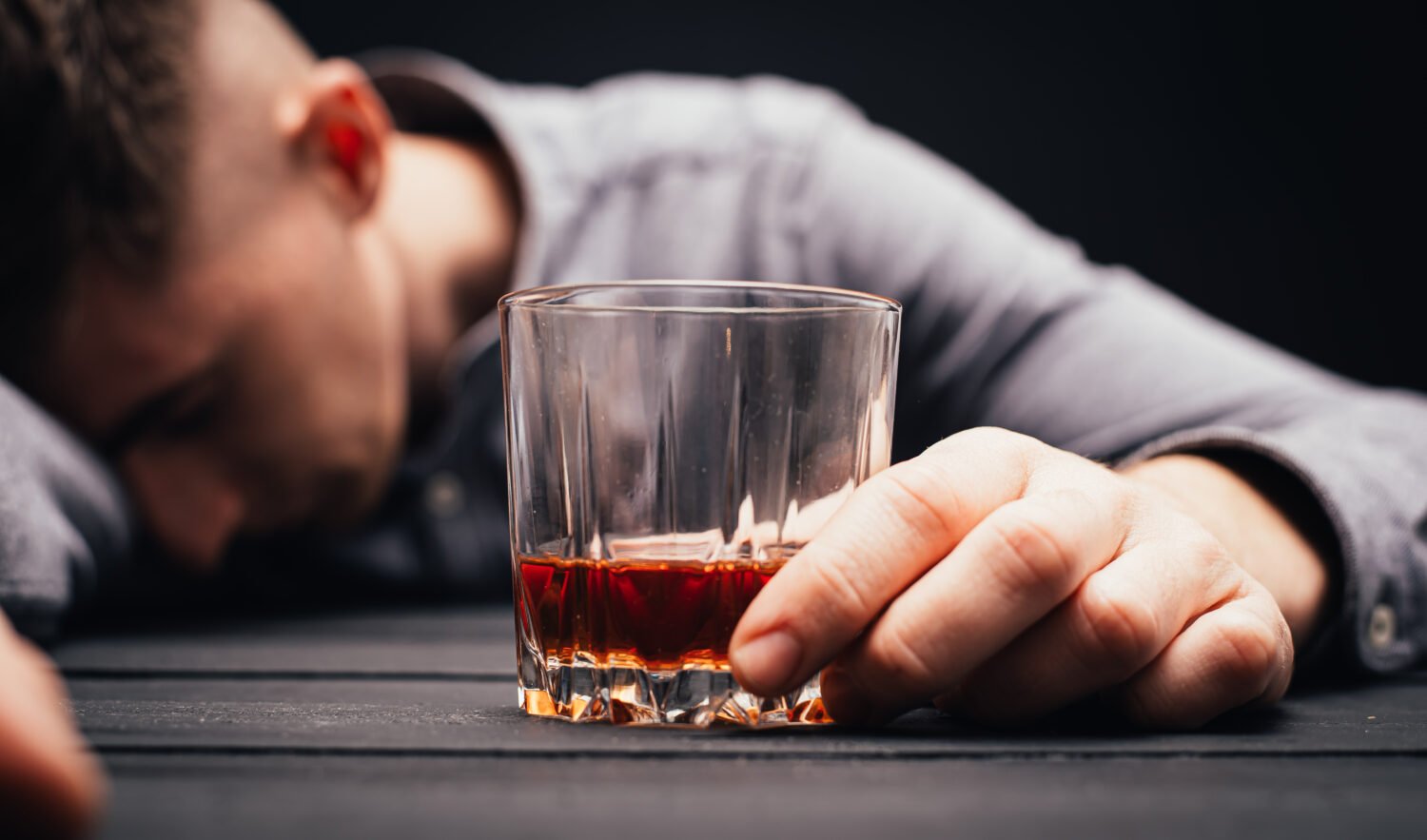 Unconscious drunk man with glass of whiskey at table