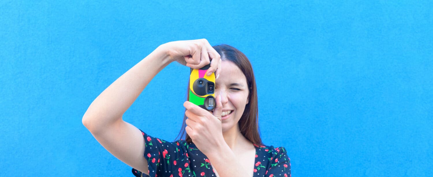 Funny caucasian girl in casual outfit is taking a pictures with a vintage camera outdoor - Summer, joy, relax, concept - close up portrait, coloured background with a space for advertising