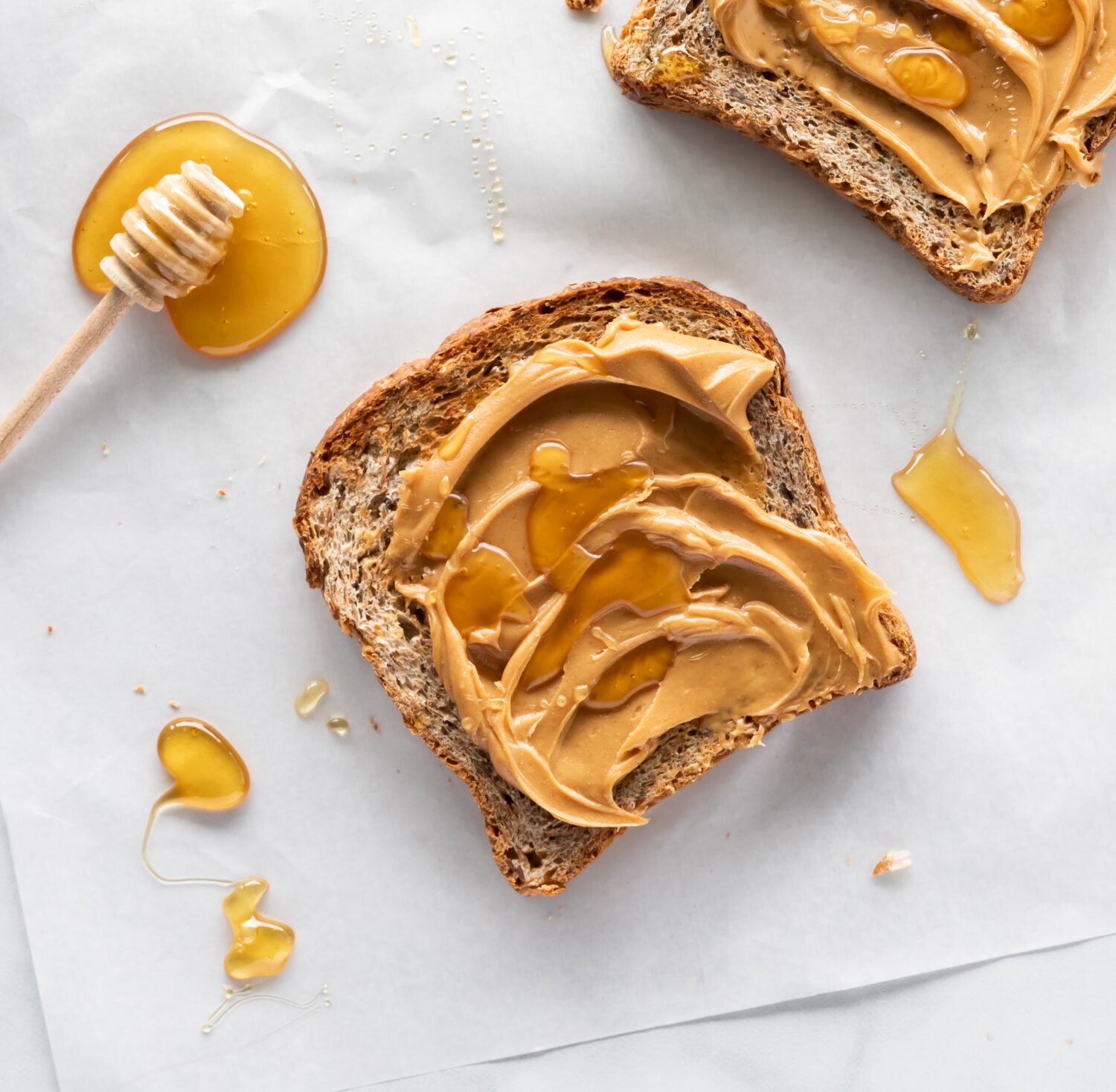 Close up view of a piece of toast covered with creamy peanut butter and honey, ready for eating.