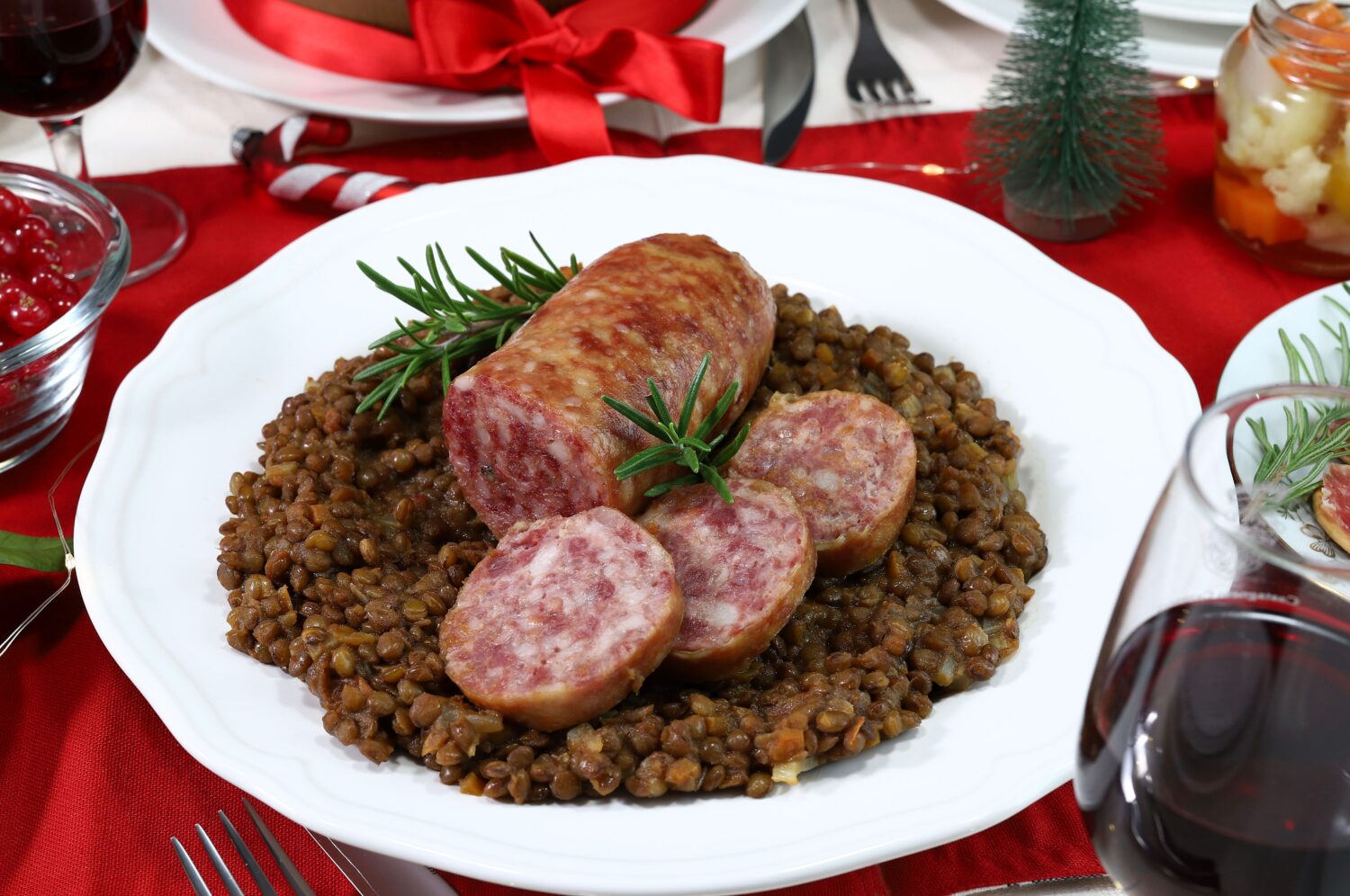 Traditional Italian Christmas food. Cotechino with lentils, appetizer, fruits, red wine and Panettone. Family gathering concept. Directly above.