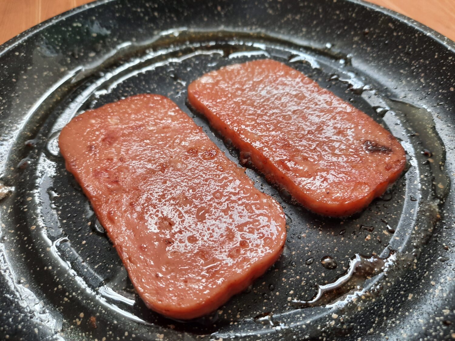 Two pieces of spam on a frying pan