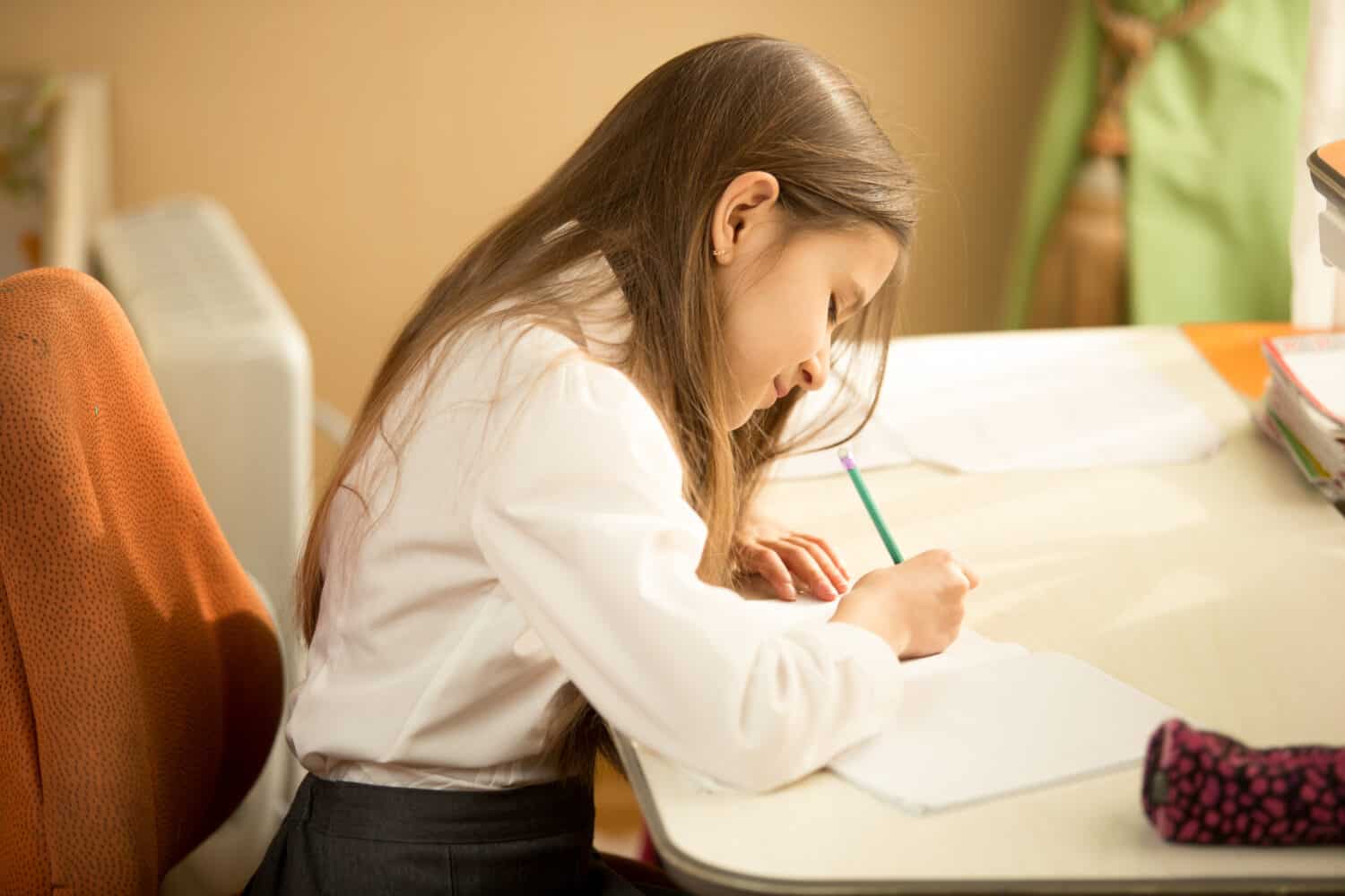 Girl writing in notebook with pencil at her bedroom