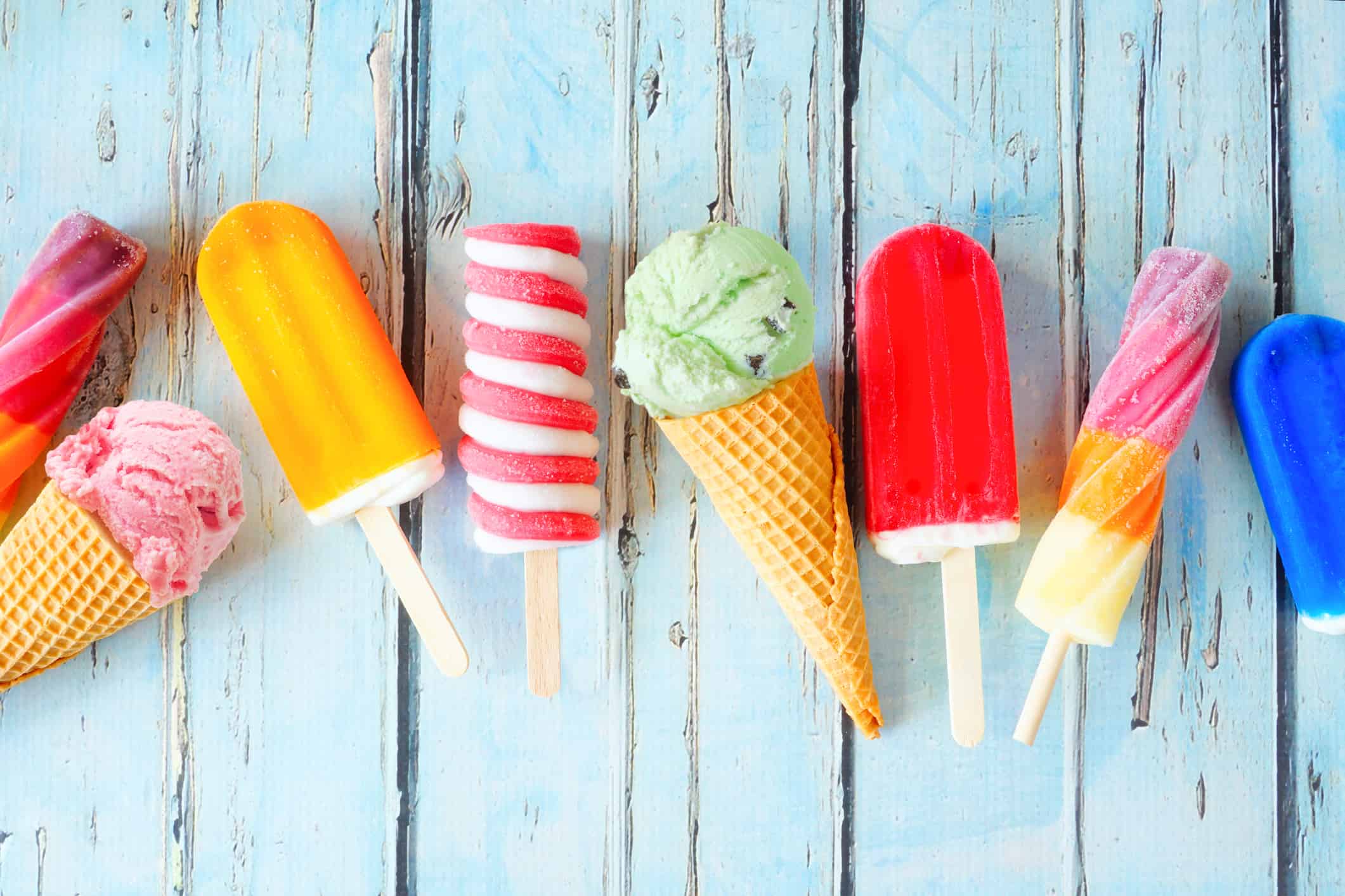 Selection of colorful summer popsicles and ice cream treats scattered on rustic blue wood
