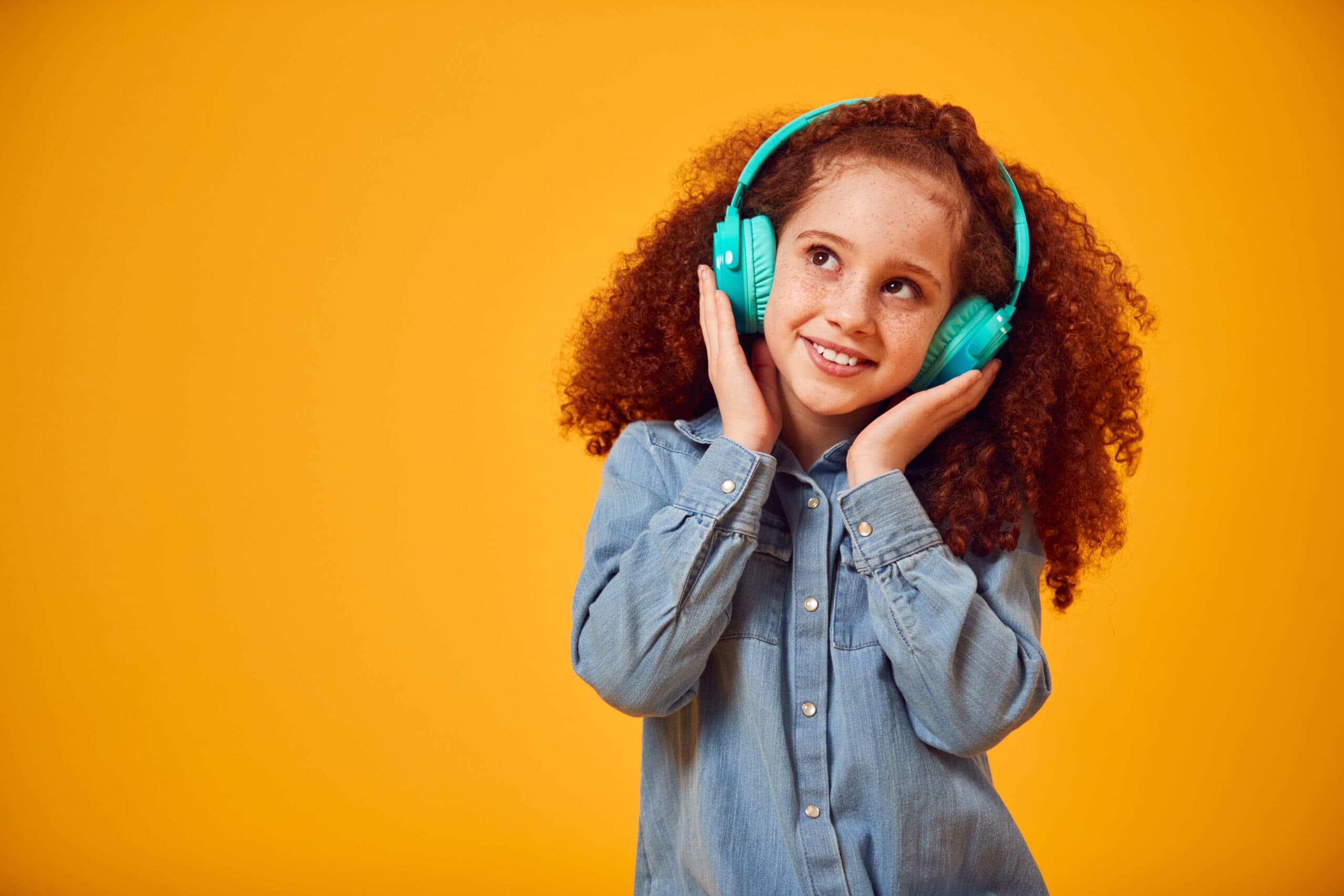 Studio Shot Of Smiling Young Girl Listening To Music On Headphones Against Yellow Background