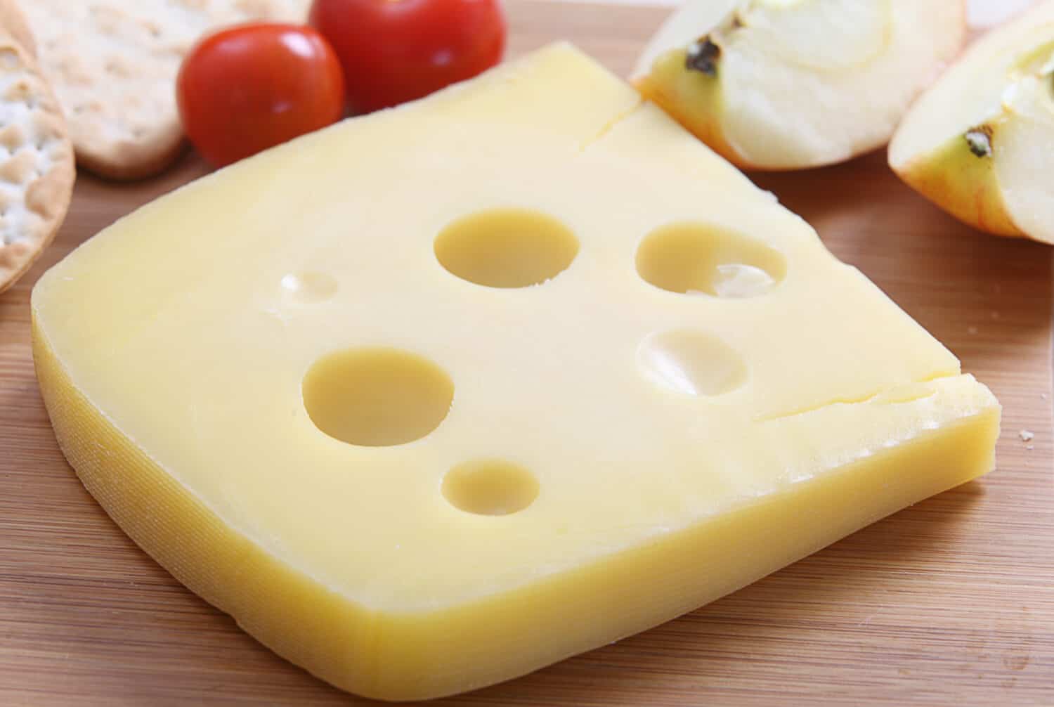 A wedge of Jarlsberg Danish cheese with crackers and cherry tomatoes on a cheeseboard