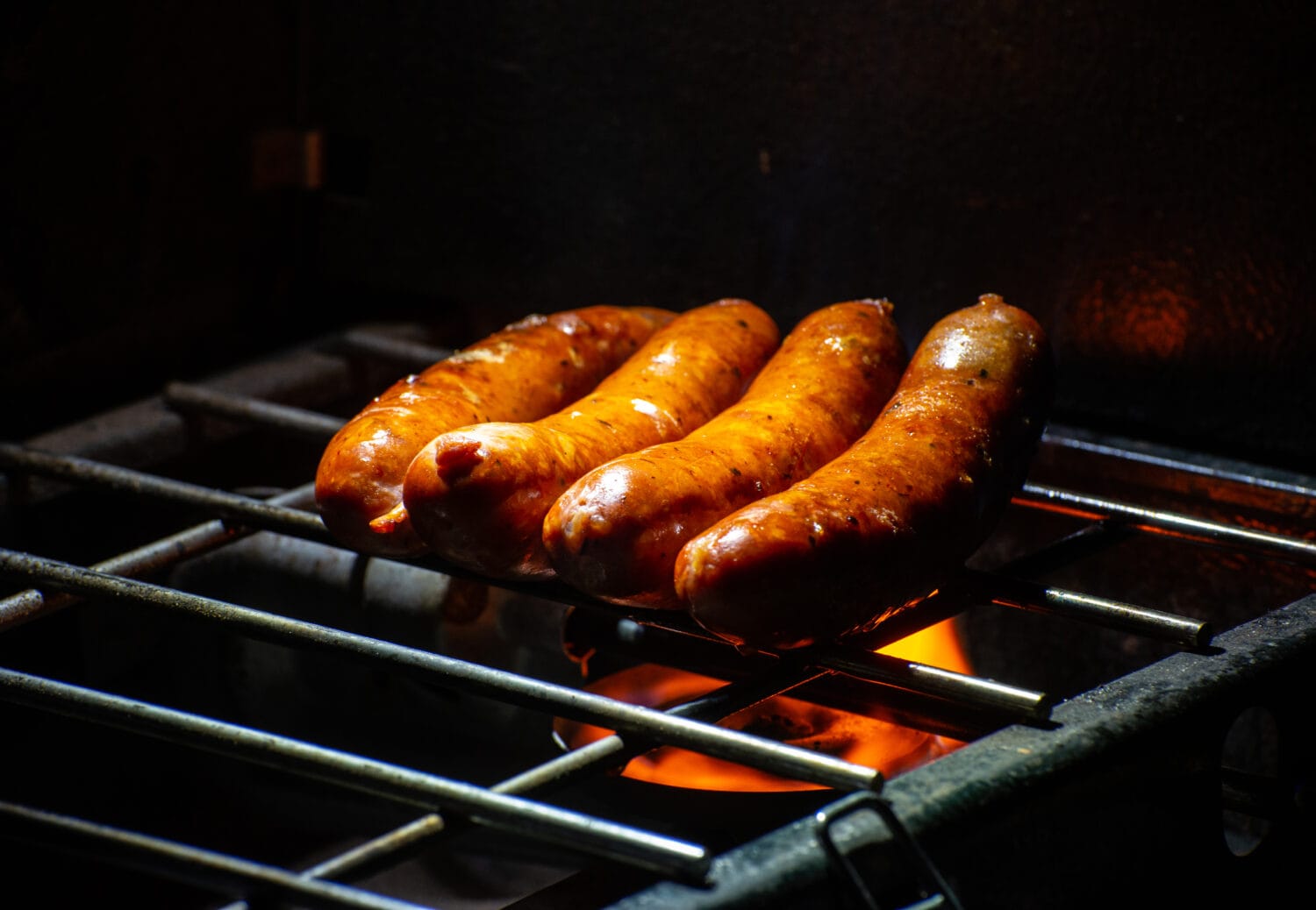 Delicious Andouille pork sausages being grilled over open flame on a camp stove with metal grill.