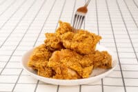 Close Up Hand and Fork on Fried Chickens on white Plate Isolated on table. Look Yummy and Yellow Gold Color.