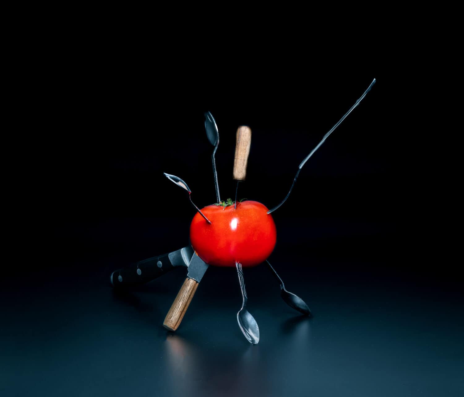 stabbed tomato with knifes, spoons and fork on black background