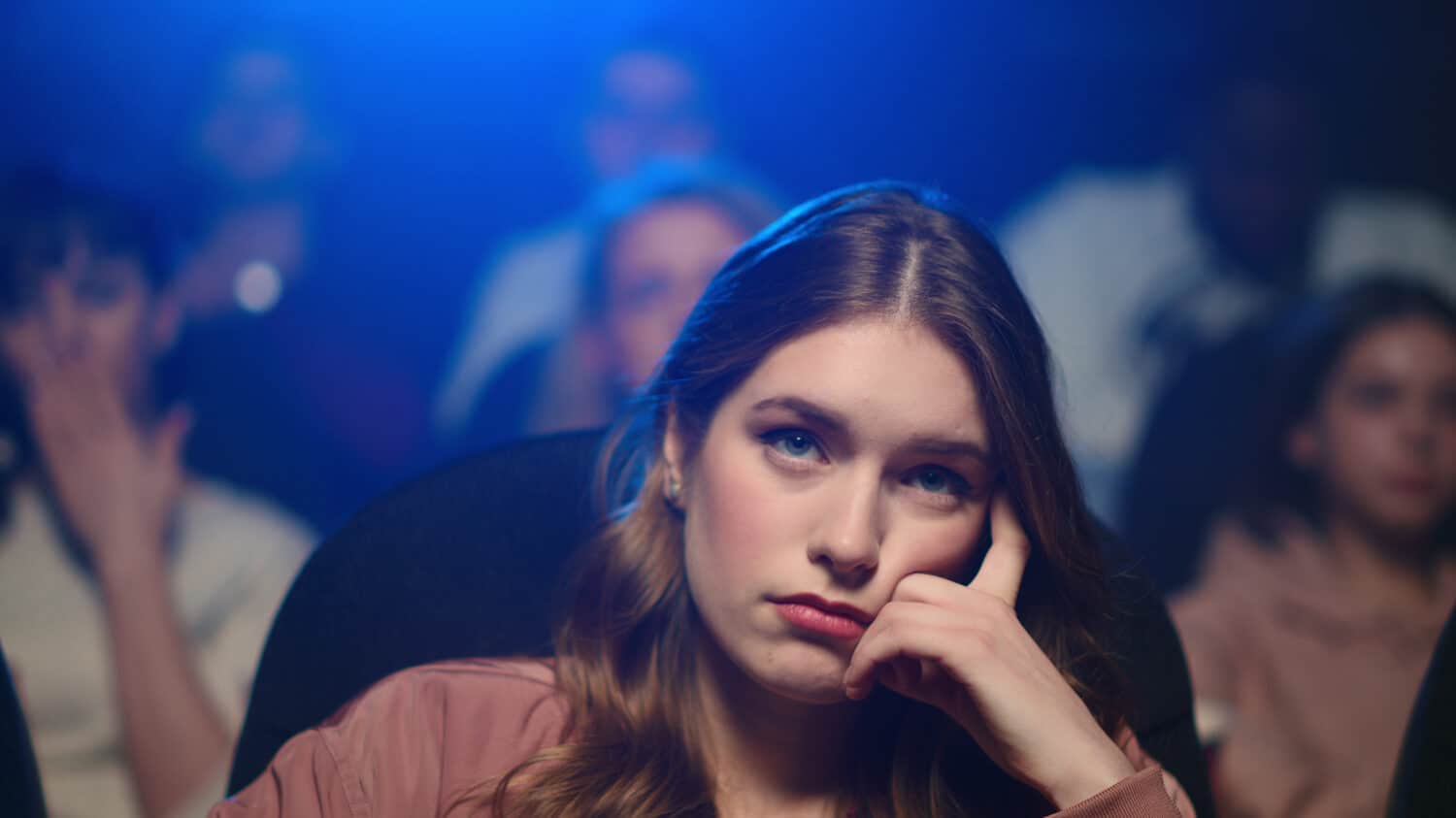 Portrait of disappointed woman watching boring film in movie theater. Closeup bored girl yawning at bad movie session. Frustrated female person sitting in cinema.