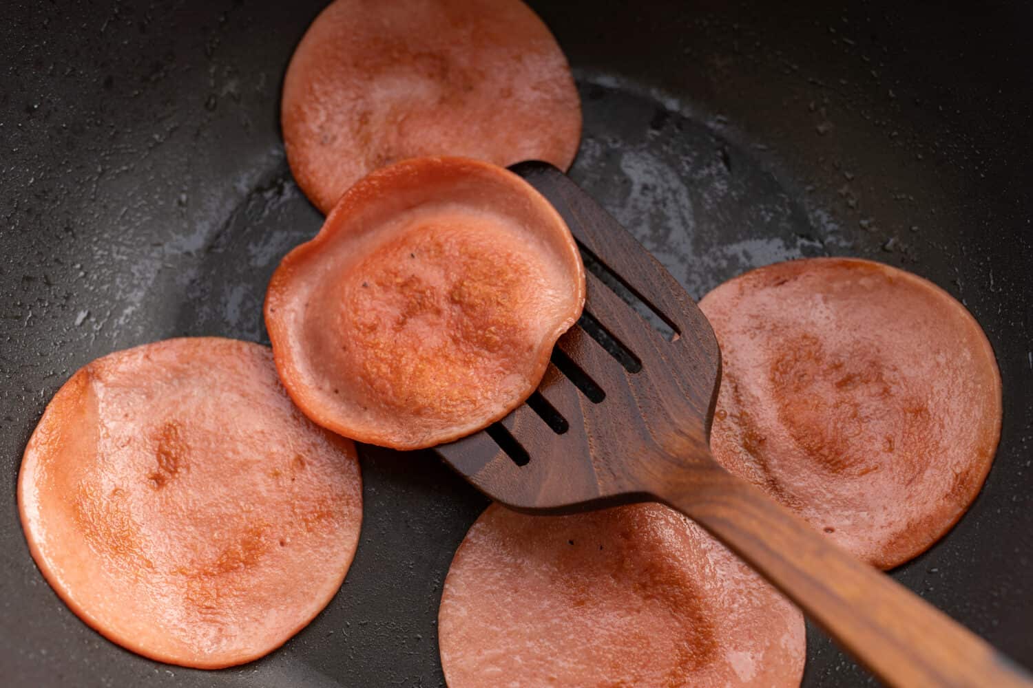closeup frying pork bologna in black pan with small amount of cooking oil
