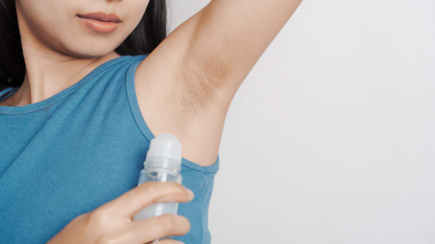 Use a roll-on to deodorize the musty smell from sweat. Young confident asian chinese female armpit with blue tank top isolated background.