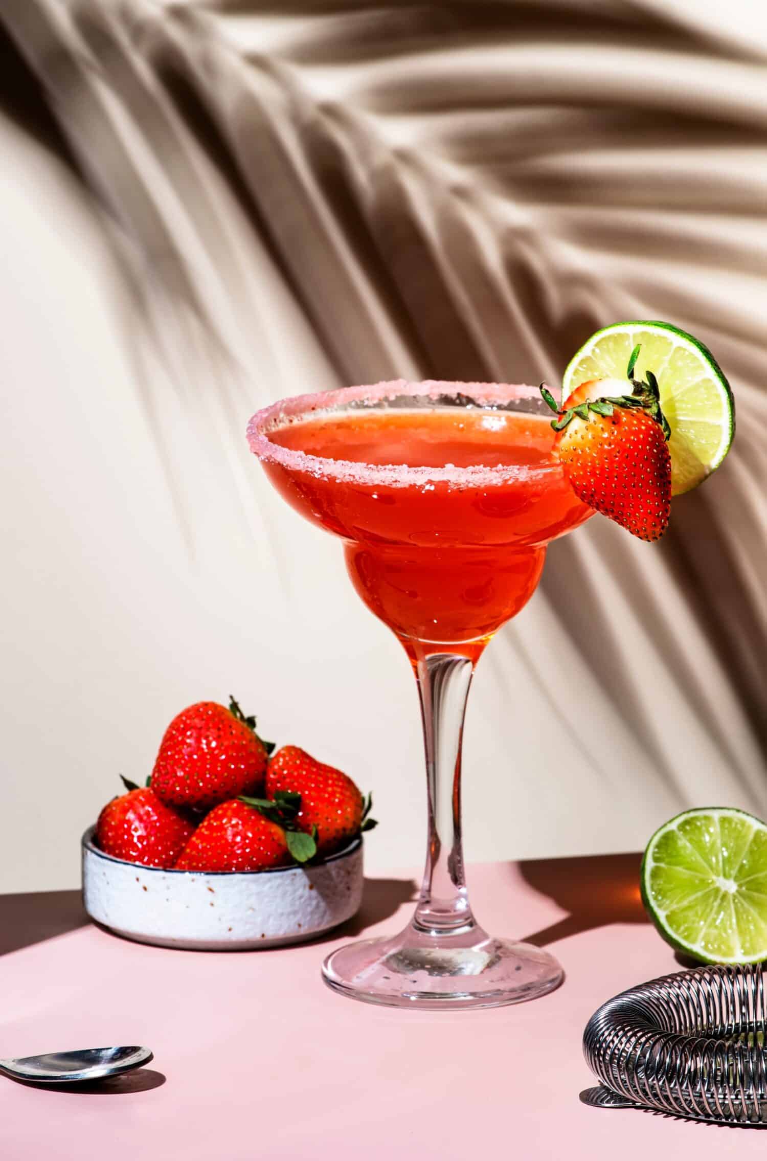 Strawberry Margarita summer cocktail drink with silver tequila, lime juice, liqueur, fresh berries and ice in glass with salt rim. Beige pink background., hard light, shadow pattern
