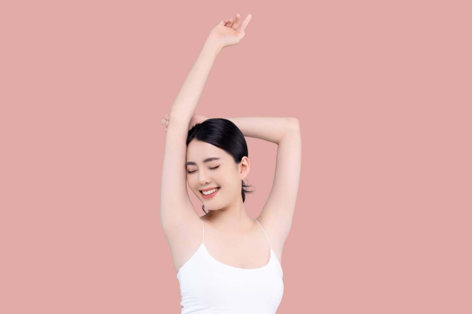 Beautiful young Asian girl lifting hand up to shows off clean and clear armpit or underarms isolated on pink background, Smooth and freshness armpit concept.
