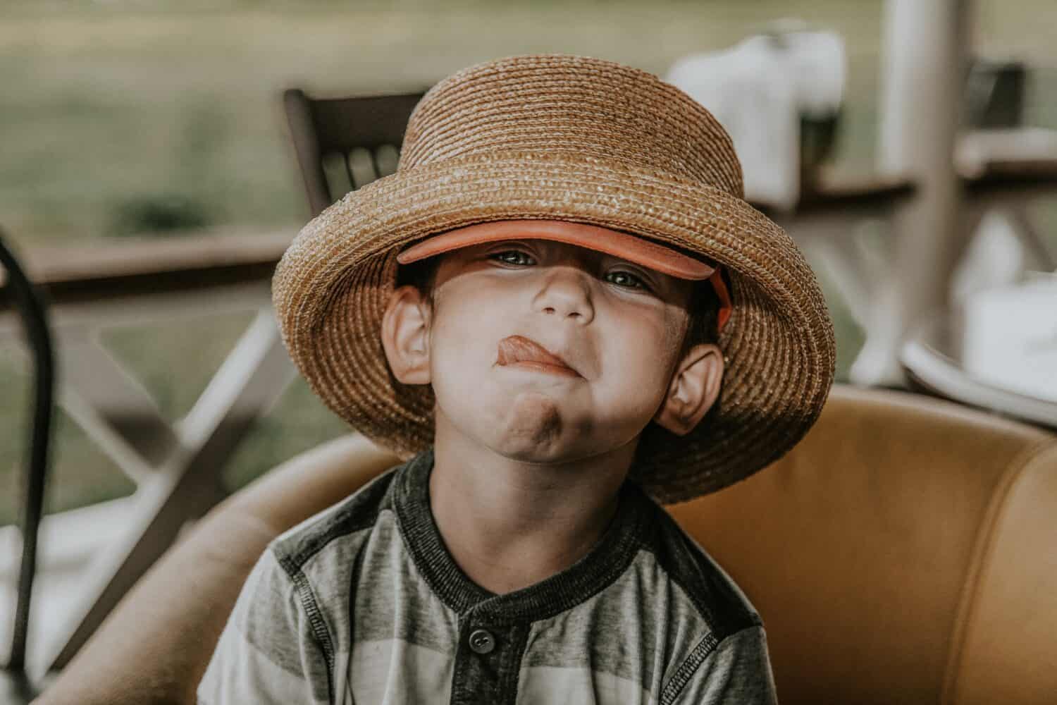 A child in a straw hat is sticking out his tongue and looking at the camera. Soft selective focus