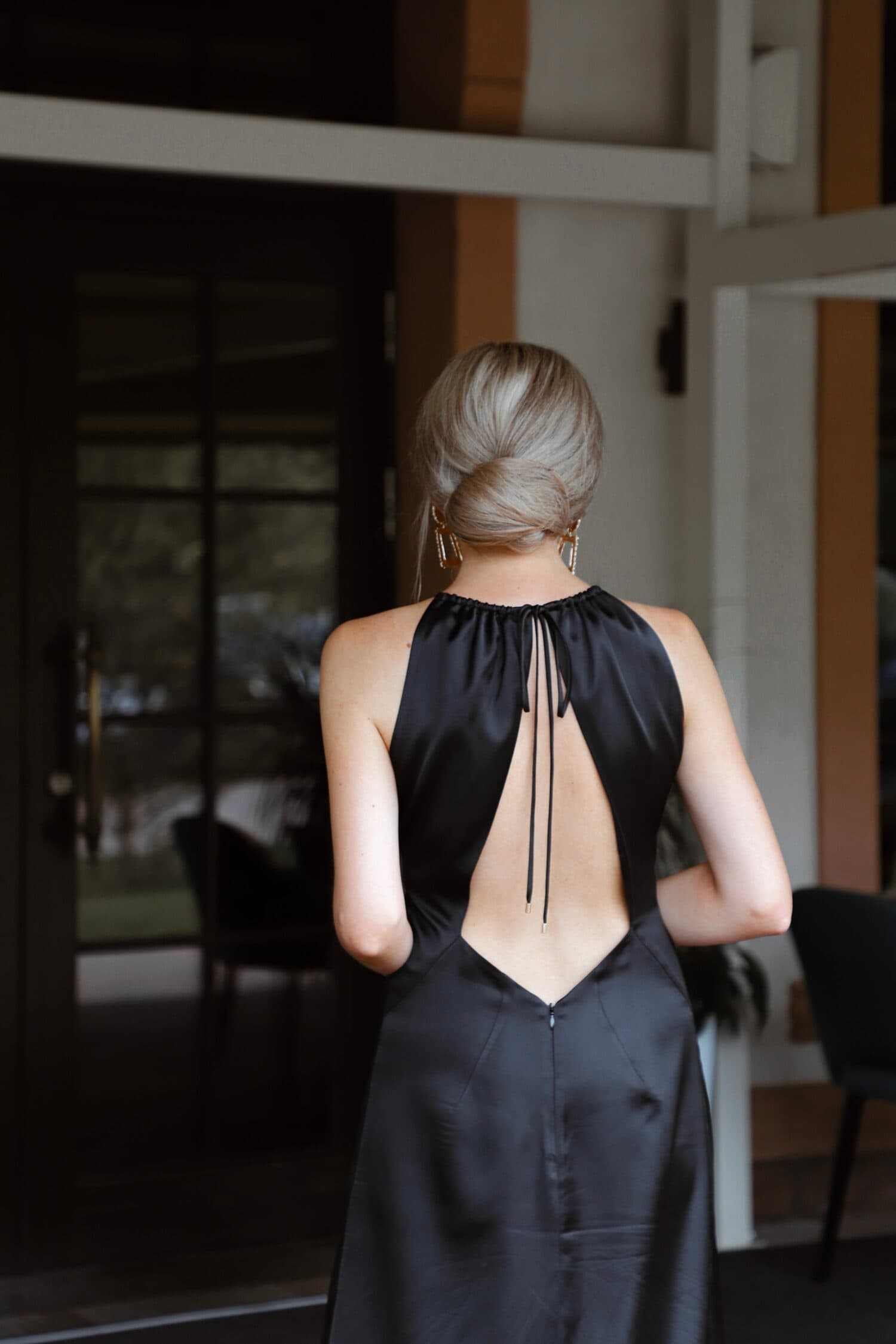 portrait of beautiful blonde girl dressed in elegant midi black dress with open back, white shoes and bag, accessories, hair gathered, festive evening outfit, lifestyle model