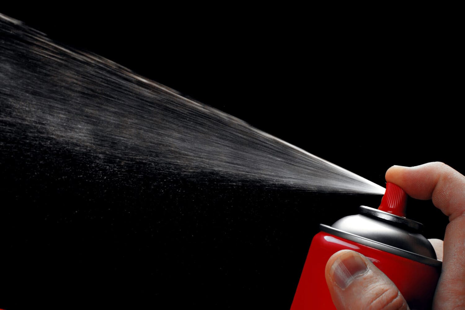 Close-up of red aerosol can showing off the spray against black background