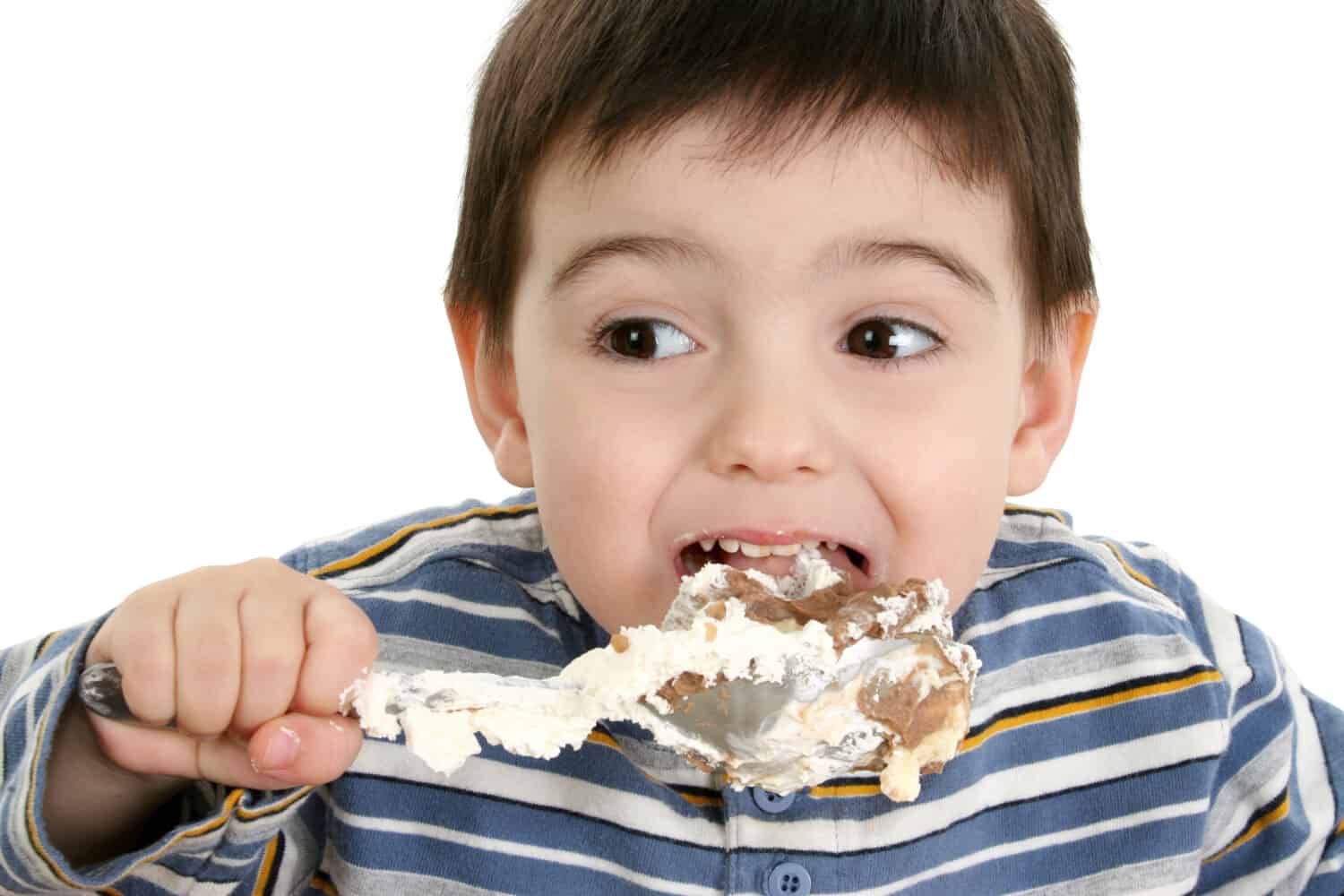 Close up of a two year old boy eating possum pie with a big silver spoon. Shot in studio over white.