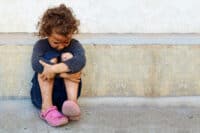 poor, sad little child girl sitting against the concrete wall