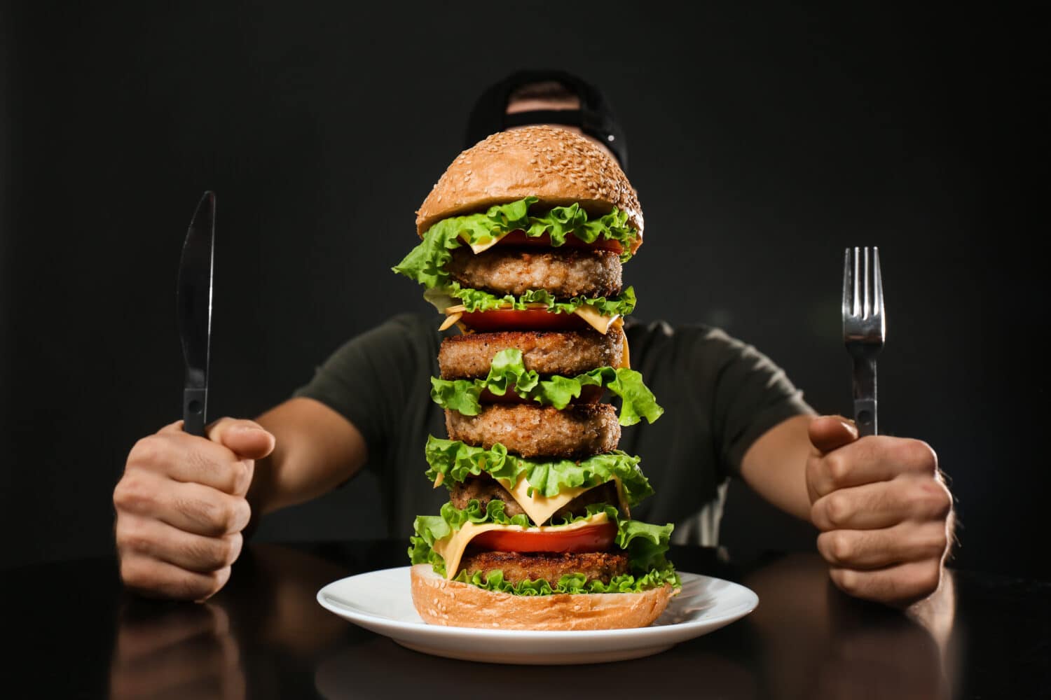 Man with cutlery eating huge burger on black background