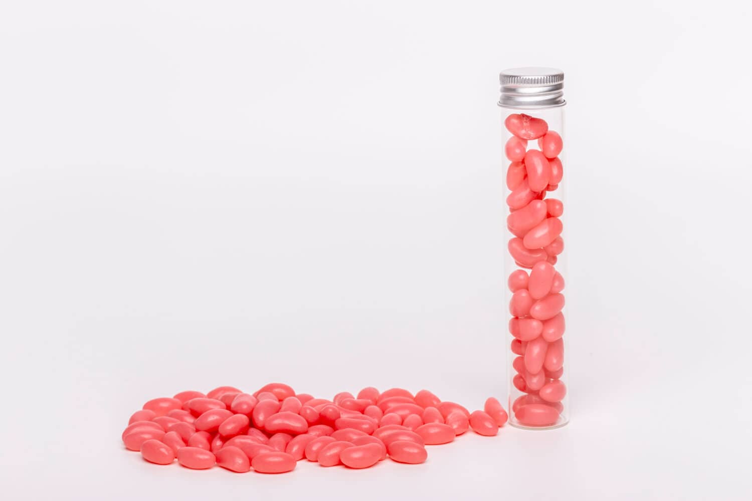 Pink jelly beans in a test tube jar with loose beans on a white background