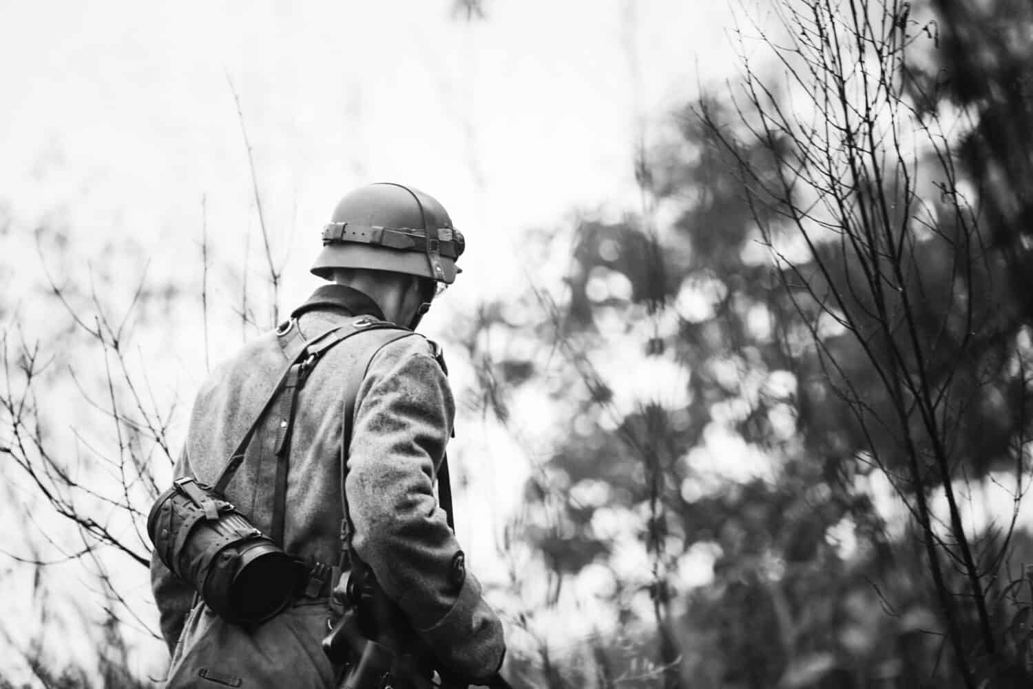 Close Up Single Re-enactor Dressed As German Wehrmacht Infantry Soldier In World War II Walking In Patrol Through Autumn Forest. WWII WW2 Times. Photo In Black And White Colors.