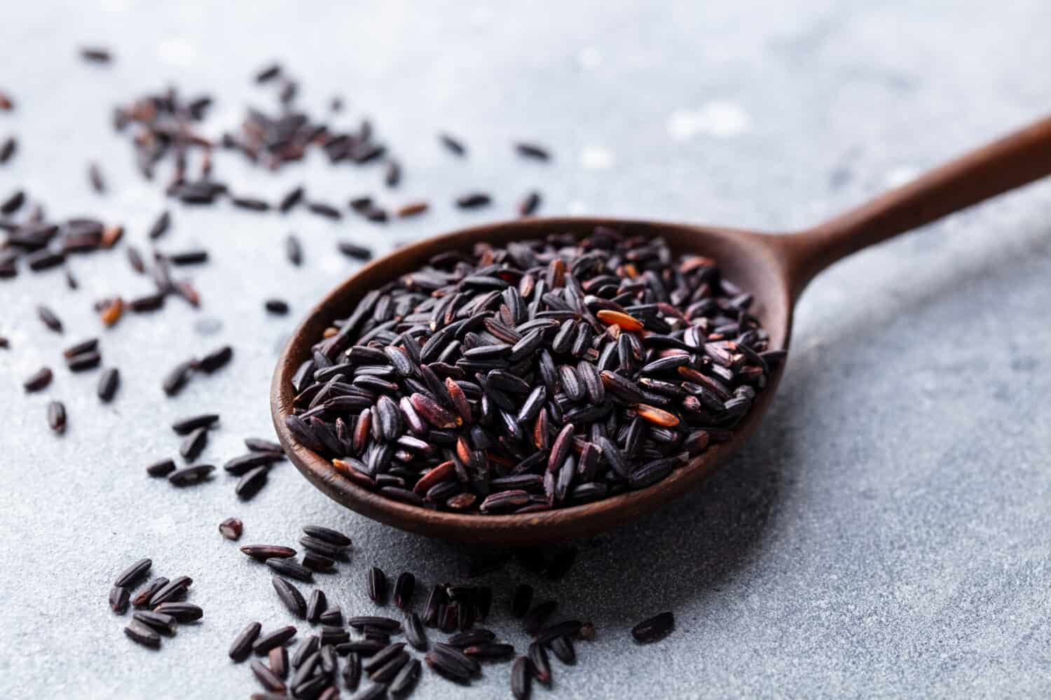 Black wild rice in a wooden spoon. Grey stone background. Close up.