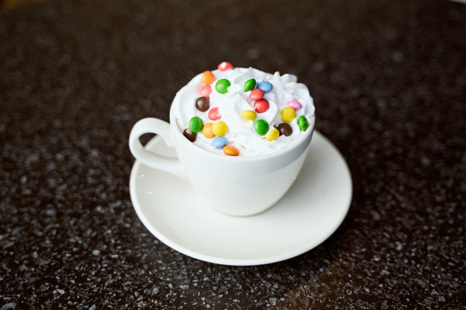 coffee cacao in a paper cup with whipped cream and candy on a table