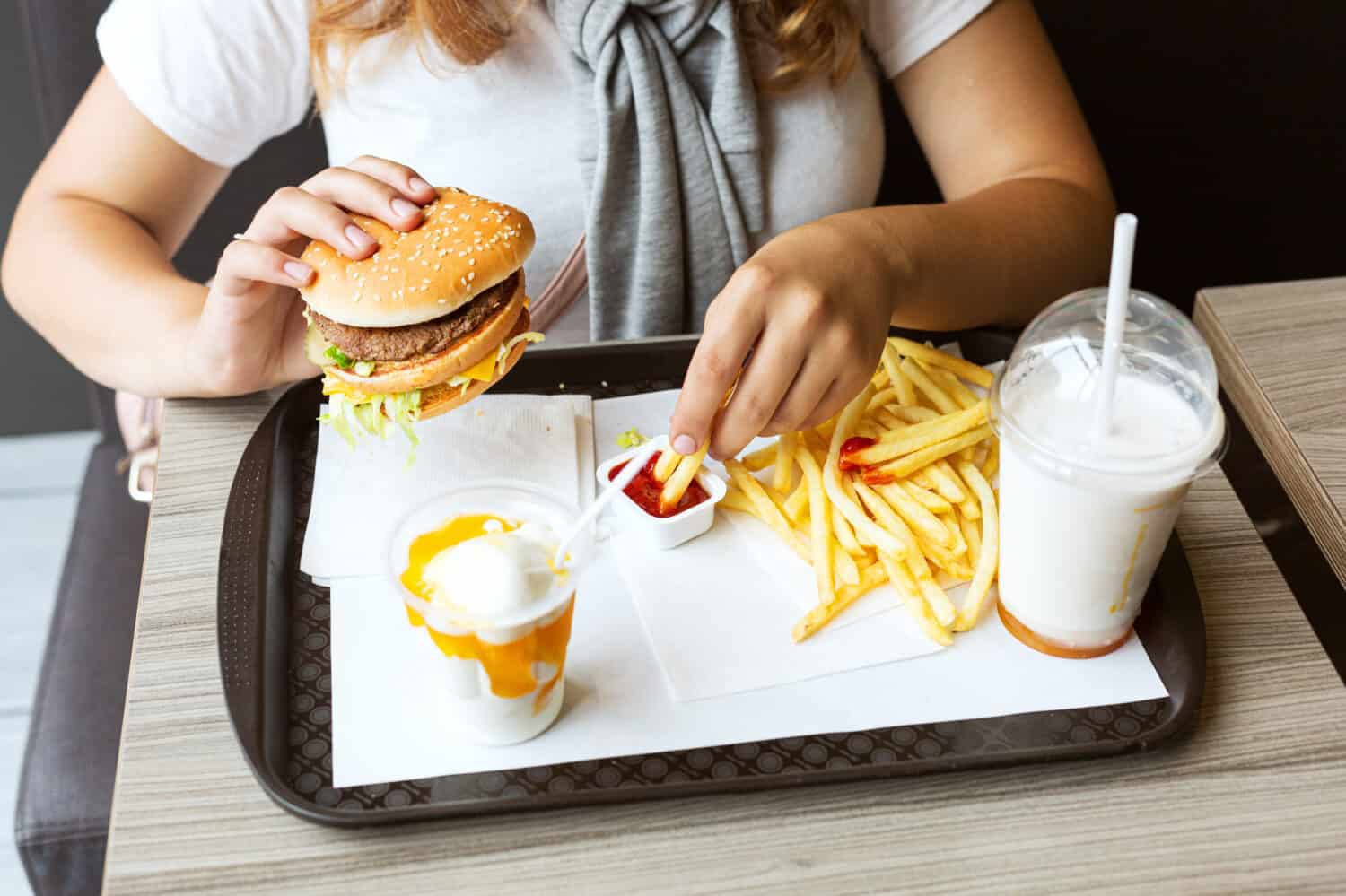 Junk food is comfort food. Woman holds in her hand hamburger and fries with ketchup. Concept: fatty, high-calorie, unhealthy food. Close-up. Top view