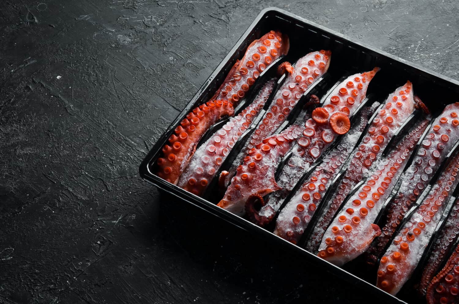 Frozen octopus tentacles in a plastic box. Top view. Flat lay.
