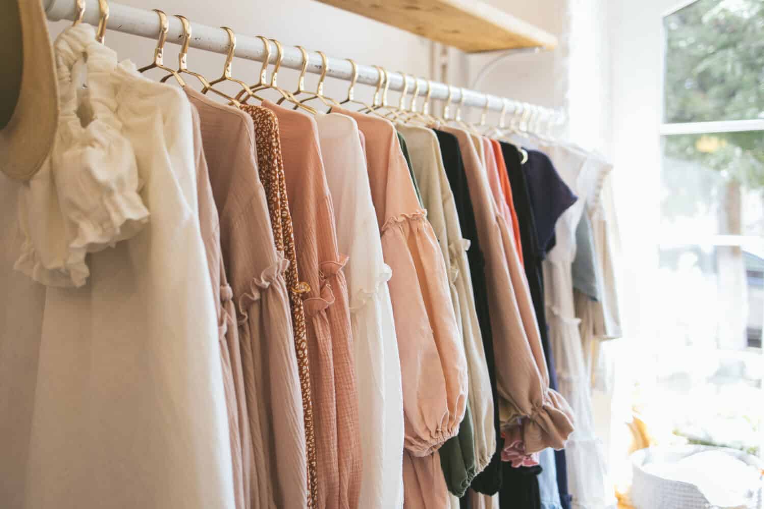 Beautiful female wardrobe. A lot of party dresses hanging on hangers in closet. Vintage clothing rental concept. Women's space. Boho market. Small boutique showroom fashion shop. big choice