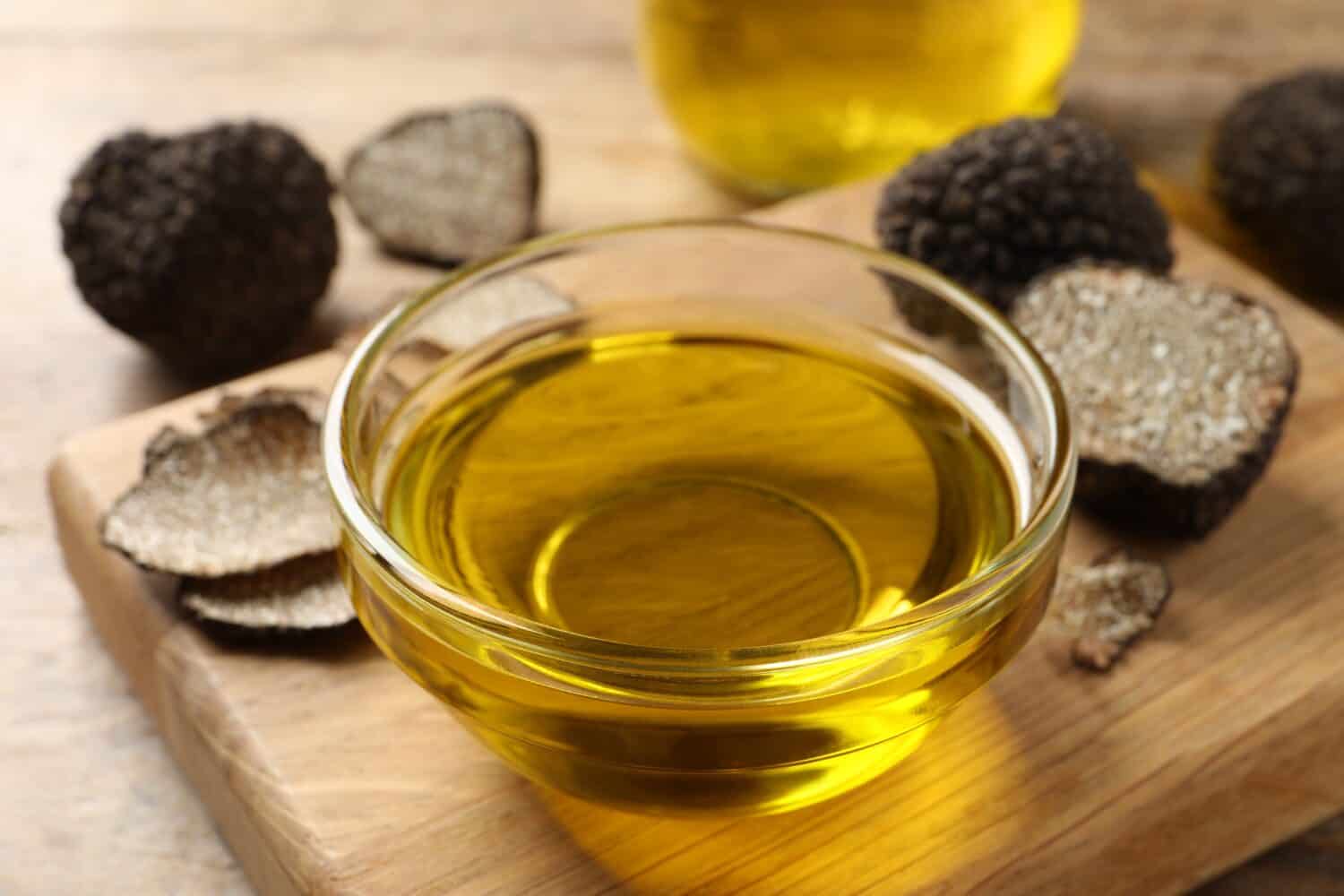 Glass bowl of truffle oil with wooden board on table, closeup