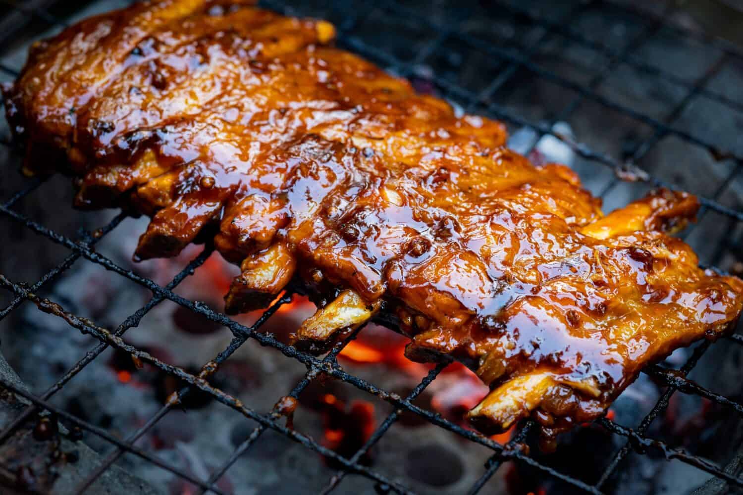 Pork ribs being grilled on smouldering charcoal