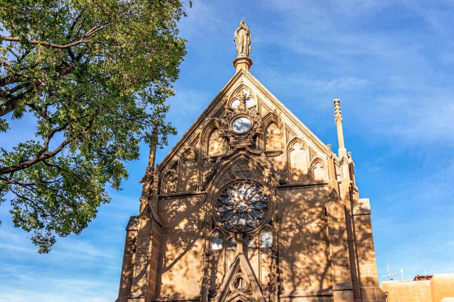 The Loretto Chapel historic old church in Santa Fe, New Mexico in United States with closeup of exterior facade and tree shadow on sunny day against blue sky with nobody