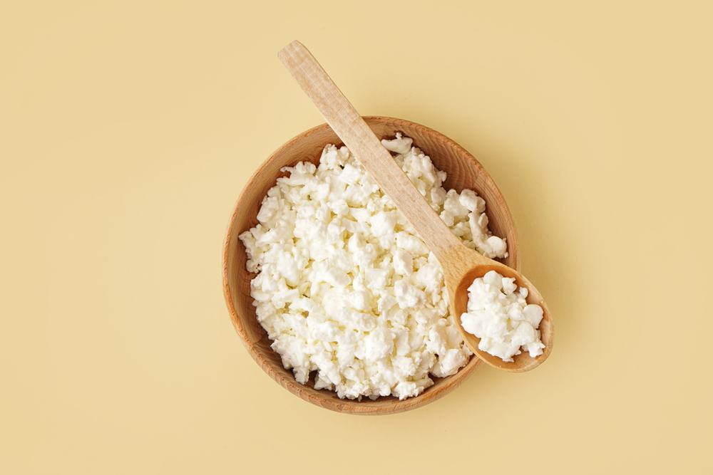 Bowl and spoon with tasty cottage cheese on yellow background