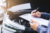 Auto check, car service shop concept. Automobile repairman writing job checklist on clipboard, mechanic checking engine to estimate repair machine, inspecting maintenance by engineer at vehicle garage