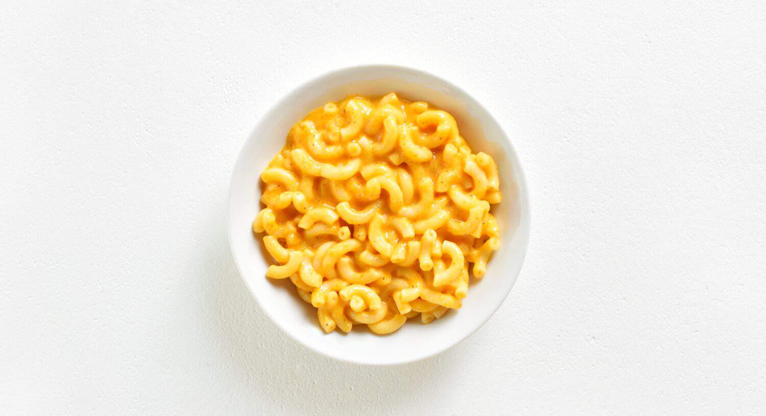 Macaroni and cheese in bowl over white background with copy space. Top view, flat lay