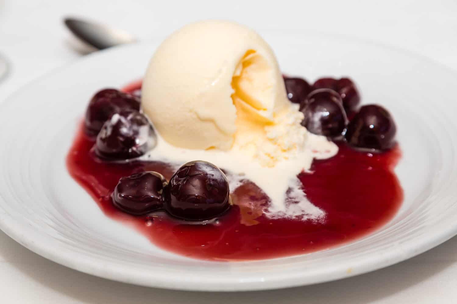 A bowl of cherries jubilee topped with a scoop of vanilla ice cream