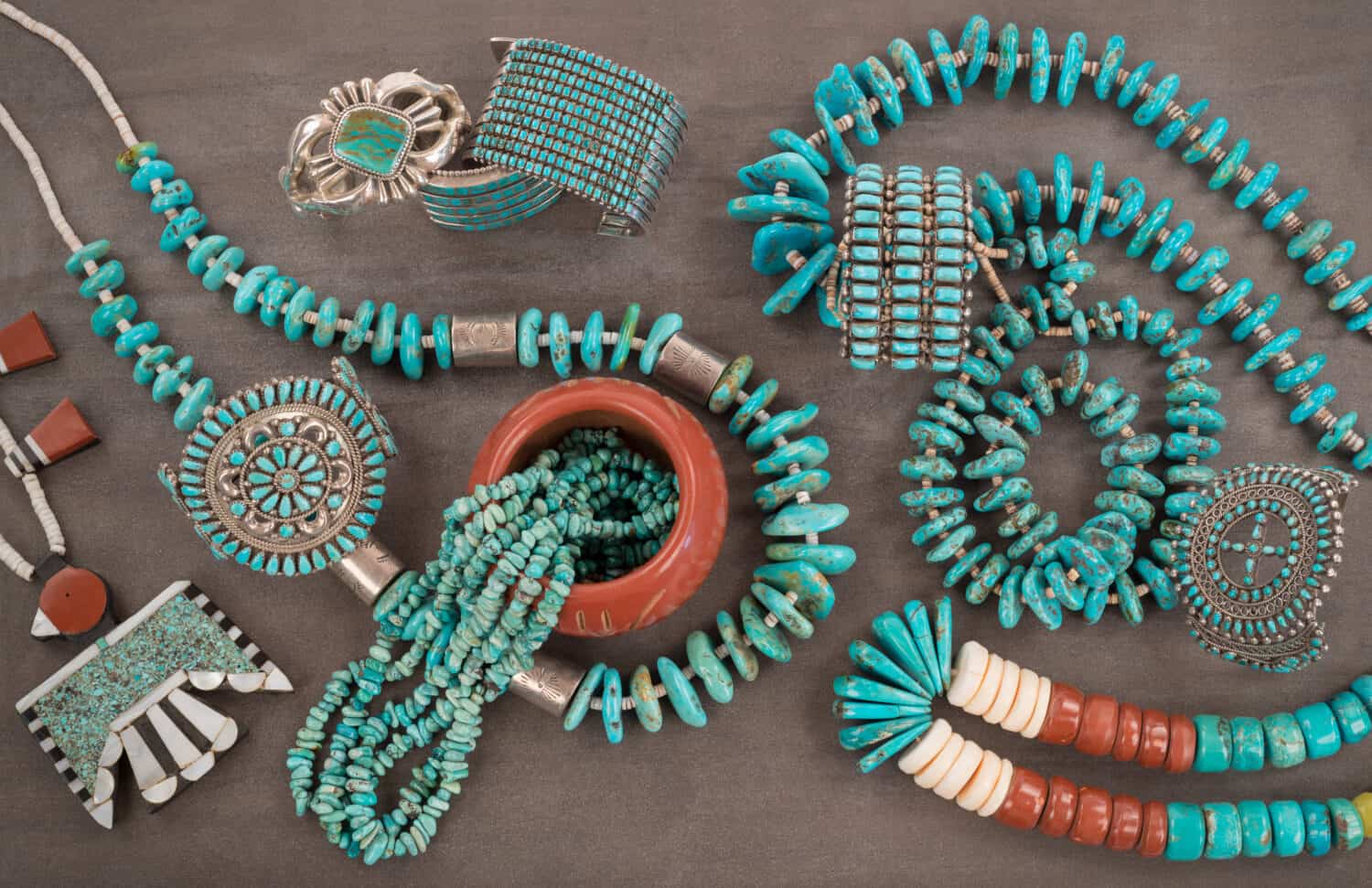 A collection of Native American Jewelry.A Santo Domingo Depression Era� Necklace, and Turquoise "Nugget" with silver beads, and Zuni and Navajo "Cuff" Bracelets, on a Grey Slate Background.