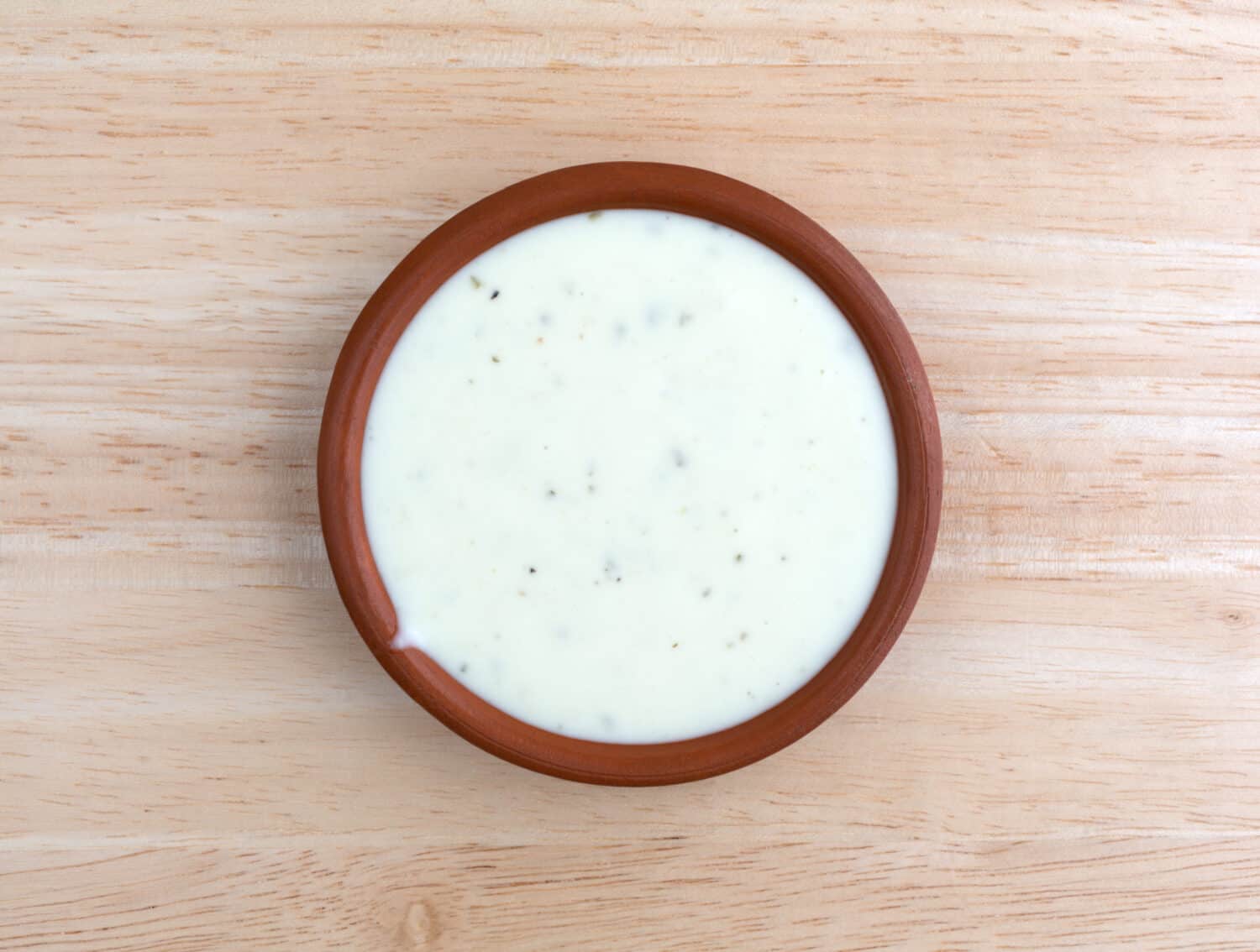 Top view of a small bowl of ranch dressing on a wood table top illuminated with natural light.