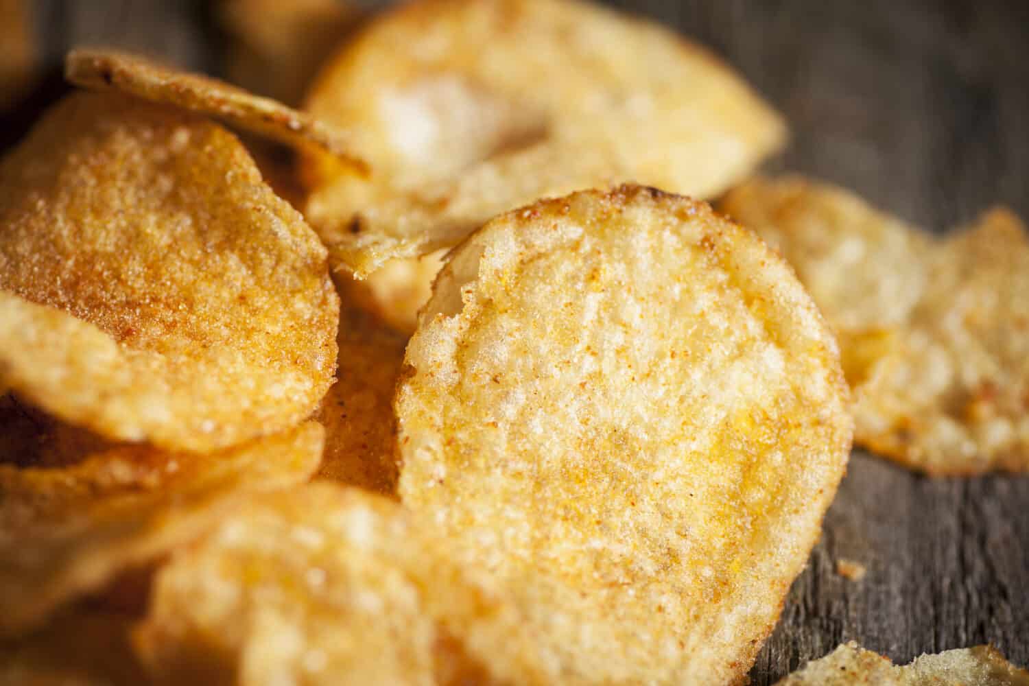Potato kettle chips/crisps scattered on a textured wooden background. Close up macro shot