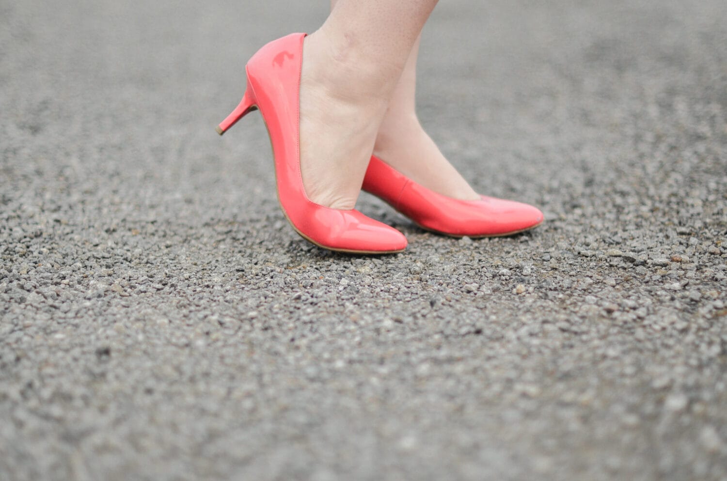 Closeup of woman wearing coral pink heels posed on gravel road