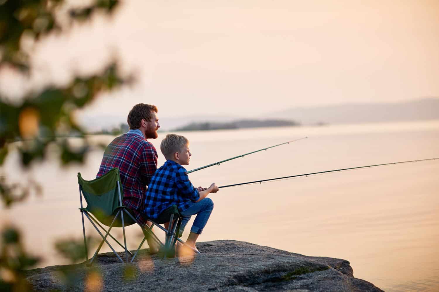 Side view portrait of father and son sitting together on rocks fishing 